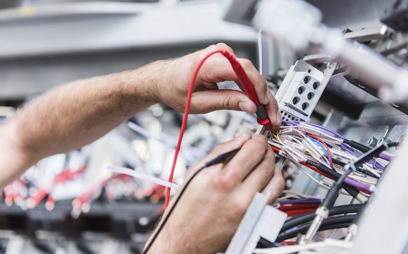 Técnico medindo a fiação de um equipamento industrial com multímetro
